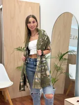 Bufanda rectangular con estampado a cuadros en tonos beige, azul y verde. Tiene flecos en los extremos y un estampado floral en el interior.