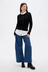 Saco de punto al cuerpo, color negro, con cuello redondo, manga larga y cierre frontal con botones pequeños.
