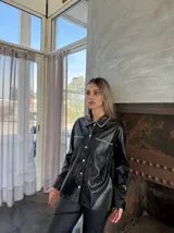 Sobrecamisa negra de cuero sintético con cuello clásico, cierre frontal con botones a presión, bolsillos con solapa en el pecho y detalle de pespuntes en contraste.