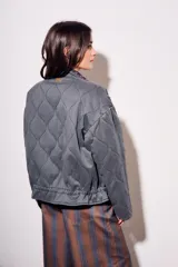 Campera acolchada gris oscuro con efecto lavado, cuello mao y cierre frontal. Presenta un patrón de costura ondulado.