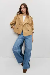 Cazadora corta de estilo gabardina en color tostado, con diseño cruzado de doble botonadura, solapas amplias, mangas largas con trabillas en los puños y hombreras.
