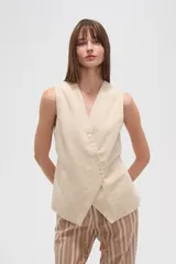Chaleco color beige claro, sin mangas, con escote en V profundo y cierre frontal asimétrico con botones.