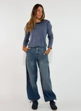 Pantalon de jean estilo wide leg con diseño de tiro medio, bolsillos laterales y detalle de costura horizontal a la altura de la cadera que genera un efecto de volado sutil.