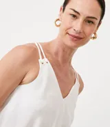 Blusa blanca de poliéster con escote en pico, tirantes finos ajustables y corte cruzado.