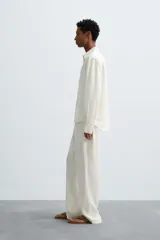 Camisa de corte relajado confeccionada en tejido de cáñamo, color blanco. Presenta cuello de solapa, manga larga con puños abotonados y cierre frontal de botonadura.