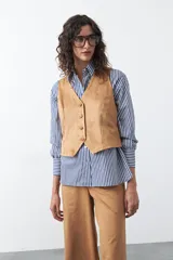 Chaleco de gamuza color tostado, con escote en V y cierre frontal con botones forrados. Tiene un diseño limpio y silueta definida, con largo a la cintura.