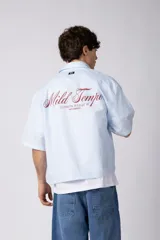 Camisa de manga corta de popelina rayada, con calce boxy y bordado sutil en el pecho. Presenta cierre frontal con botones y diseño abierto.