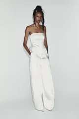 Top palabra de honor de tejido satinado blanco, con escote recto y diseño con bajo tipo peplum y costuras marcadas.