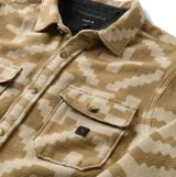 Camisa de franela Roark modelo Nordsman Jacquard, de corte recto y manga larga. Presenta un estampado geométrico inspirado en textiles tradicionales en tonos marrón y beige, con cierre frontal de botones a presión y dos bolsillos con solapa en el pecho.