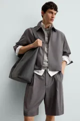 Bermuda de corte relajado color negro, con pliegues frontales, cierre de cremallera y botón, bolsillos laterales y bolsillos traseros.