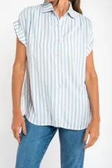 Camisa oversize celeste y blanca a rayas verticales, con cuello clásico, mangas cortas con dobladillo y cierre frontal con botones.