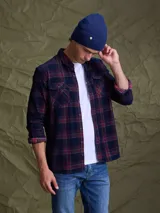 Camisa de manga larga con diseño a cuadros en tonos azul marino y rojo. Presenta cuello clásico, cierre frontal con botones y dos bolsillos en el pecho con solapa.