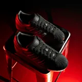 Championes Adidas modelo Superstar, color negro con las icónicas tres tiras laterales en acabado iridiscente y puntera de goma clásica.