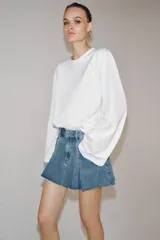 Falda corta de tiro medio confeccionada en tejido denim de algodón. Presenta diseño con tablas, bolsillos delanteros, cintura con trabillas y bajo desflecado. Cierre frontal con cremallera, botón y ganchos metálicos.
