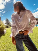 Camisa marrón de algodón con cuello clásico, cierre frontal con botones dorados y mangas largas abullonadas con puños elásticos.