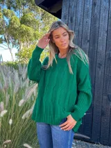 Buzo verde de lana y poliamida, con diseño oversize, cuello redondo y trenzas en la parte delantera.