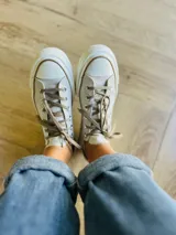 Zapatillas bajas de lona color blanco, con cordones marrones, puntera de goma y base blanca.