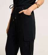 Pantalón negro de crepé con corte carrot, cintura alta con elástico en la parte trasera y lazo en la delantera, bolsillos delanteros con detalle metalizado y bolsillos cargo laterales.