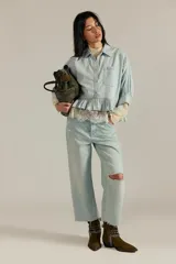Camisa de denim de corte oversize, color celeste, con bolsillos frontales, mangas abullonadas y detalle de volados en el ruedo.