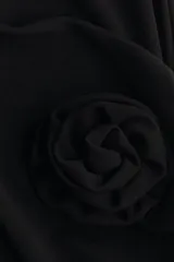 Vestido corto de punto color negro, con cuello alto, mangas largas con hombreras y corte ajustado. Presenta un panel delantero en la cadera con un aplique de rosa y una tira larga lateral.