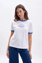 Remera blanca de manga corta con cuello redondo y ribete en color azul. Presenta un estampado central en azul con texto en francés que hace referencia a una dirección en París.