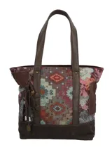 Cartera tipo tote de hombro con diseño patchwork en tonos marrones, burdeos y celestes, combinando patrones geométricos y florales. Presenta detalles en cuero sintético marrón, asas fijas y un llavero colgante con borla y abalorios.