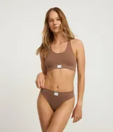 Bombacha bikini hilo color marrón, confeccionada en poliamida con tecnología seamless y textura acanalada. Presenta cintura mediana y es biodegradable.