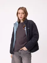 Campera puffer reversible de la marca Rusty, con diseño capitoneado. Presenta cuello alto, cierre frontal completo y logo bordado en el pecho. El interior es de un tono contrastante.