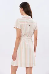 Vestido corto de lino con diseño de rayas verticales en tonos rosado, celeste, verde y beige. Presenta cuello camisero, mangas cortas, cierre frontal con botones y un lazo ajustable en la cintura.