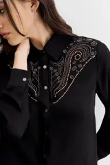 Camisa de estilo texano en color negro, con mangas largas, cuello camisero y cierre frontal con botones metálicos. Presenta un diseño con tachas termo fijadas en la zona del canesú delantero.