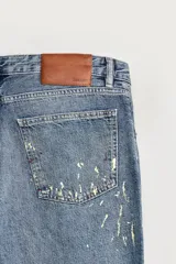 Jeans flare fit de hombre confeccionados en denim de algodón color azul con efecto lavado y roturas. Presentan diseño de cinco bolsillos, efecto salpicaduras de pintura en toda la prenda y bajo con acabado irregular.