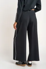 Pantalón de corte wide leg color negro, confeccionado en tejido de algodón con elastano. Presenta una franja lateral blanca a lo largo de cada pierna y cintura elástica.