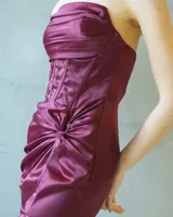 Vestido largo strapless de satén color bordó, con cuerpo estilo corsé estructurado y detalle de drapeado lateral que desemboca en una abertura frontal en la falda.