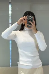 Buzo tipo polera de tejido morley, color blanco, con cuello alto y mangas largas ajustadas.
