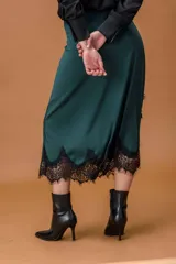Falda midi de satén en color verde oscuro, con corte irregular y detalle de encaje negro en el ruedo y en uno de los laterales.