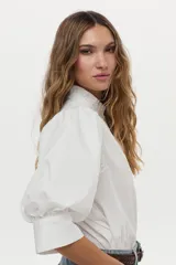 Camisa blanca de cuello mao con volados, mangas abullonadas y cierre frontal con botones.