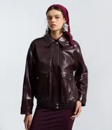 Campera bomber de poliuretano color bordó, de diseño estructurado con efecto charol. Presenta cuello clásico, cierre frontal con botones a presión, bolsillos frontales con solapa, y cintura y puños elastizados.