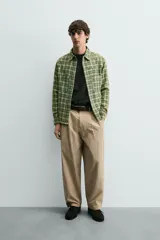 Camisa de corte relajado confeccionada en tejido de algodón con estampado de cuadros en tonos verdes y beige. Presenta cuello solapa, cierre frontal con botones a presión, bolsillos plastrón en el pecho y mangas largas con puños abotonados.