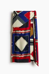 Pollera larga con diseño cruzado efecto pañuelo y brillo sutil. Presenta un estampado geométrico multicolor en tonos azul, rojo y crudo con detalles de cadenas.