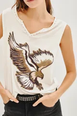 Musculosa de viscosa color blanco con escote en V y detalle de tachas en el borde del cuello. Presenta un estampado frontal de un águila en tonos tierra.