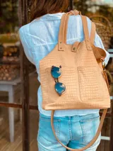 Cartera tipo tote bag color beige con textura símil cocodrilo, doble asa corta y correa larga extraíble y ajustable. Tiene dos bolsillos externos grandes y cierre superior con botón a presión.