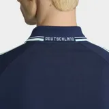 Campera deportiva Adidas de la selección de Alemania, color azul marino con detalles en celeste. Presenta cuello tipo polo, cierre frontal, bolsillos laterales y las icónicas tres tiras de la marca en las mangas. Incluye el logo del Trifolio y el escudo de la federación alemana en el pecho.