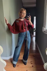 Jersey de punto color bordó con cuello asimétrico, detalle de nudo en el escote y pedrería en forma de hoja en el hombro. Manga larga.