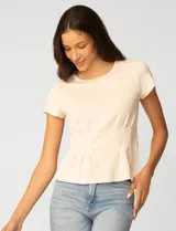 Remera blanca de manga corta con cuello redondo, confeccionada en una mezcla de modal, poliéster y elastano. Presenta un diseño con alforzas verticales en el frente que aportan estructura y una silueta relajada.