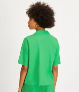 Camisa de manga corta confeccionada en mezcla de viscosa y lino color turquesa. Presenta cuello camisero con escote en V, bolsillos frontales de parche y cierre frontal con botones geométricos de efecto carey.