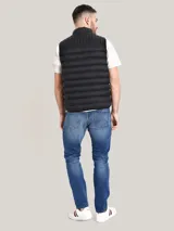 Chaleco acolchado de nailon color negro, con cuello alto, cierre frontal de cremallera con detalles distintivos de la marca y bolsillos laterales con cierre. Presenta el logo de Tommy Hilfiger bordado en el pecho.