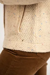 Cardigan color crema con diseño moteado en azul y naranja, de tejido de punto con textura. Tiene cuello redondo, cierre frontal con broches y bolsillos de parche.