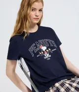 Remera de algodón color azul marino con cuello redondo y mangas cortas. Presenta un estampado frontal con el personaje Snoopy jugando al golf y la inscripción Peanuts Golf Champion 1986.