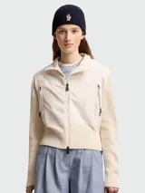 Cárdigan Moncler de algodón color blanco, con diseño acolchado en el frente, mangas de tejido de punto, cuello alto y cierre frontal con cremallera de doble sentido. Cuenta con bolsillos laterales con cierre.