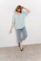 Camisa color topo confeccionada en lino, de corte holgado, con escote en V abotonado, bolsillo frontal y mangas 3/4 arremangables.